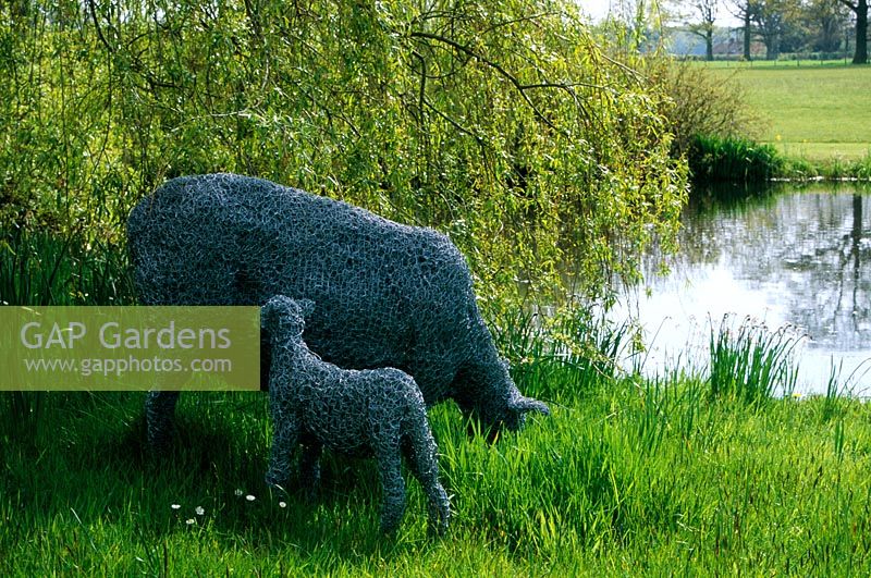 Moutons et agneaux sculptés dans du fil de poulet par étang à Old Place Farm dans le Kent