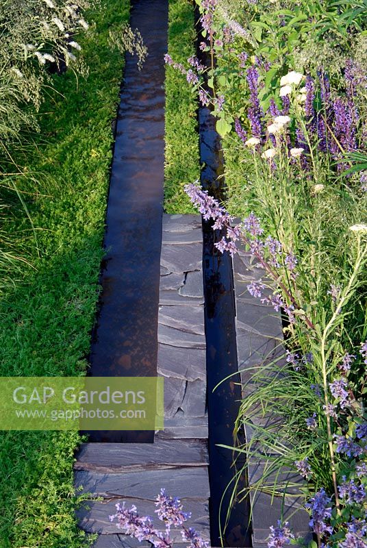 Ruisseaux d'eau bordés d'ardoise et de camomille et parterres de Salvia et d'Achillea dans le jardin 'Répétition et Différence'