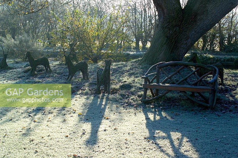 La lumière du soleil jette des ombres sur un matin glacial en hiver. Sculptures de cerfs noisetiers tissés et banc en bois
