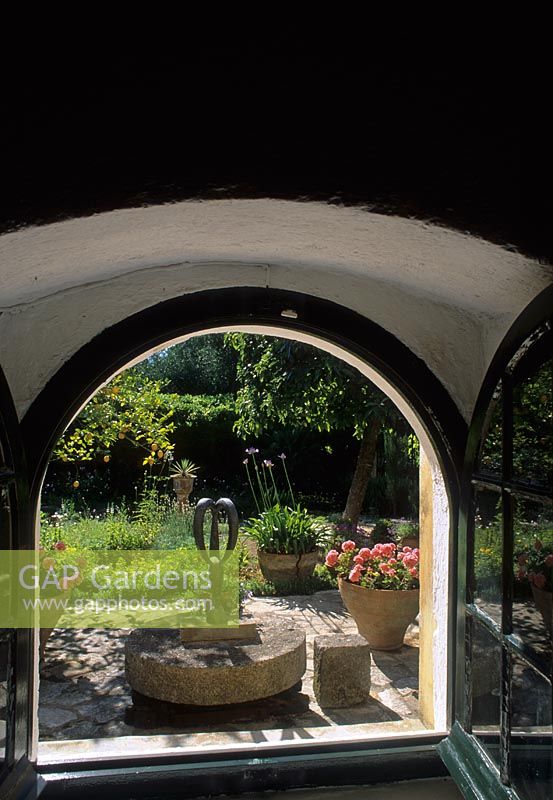 Vue à travers la fenêtre ouverte sur le jardin de style méditerranéen au-delà avec des pots et des ornements sur le patio - Corfou
