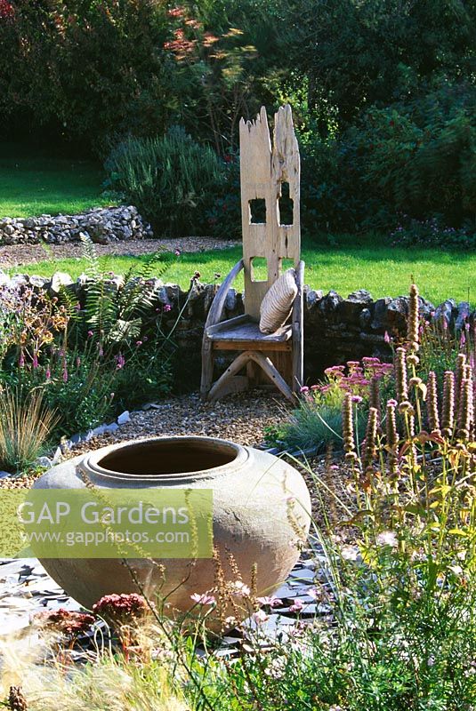 Chaise en bois trône dans le jardin de gravier avec grande urne assis sur un parterre d'ardoise cassée soulevé - Devon
