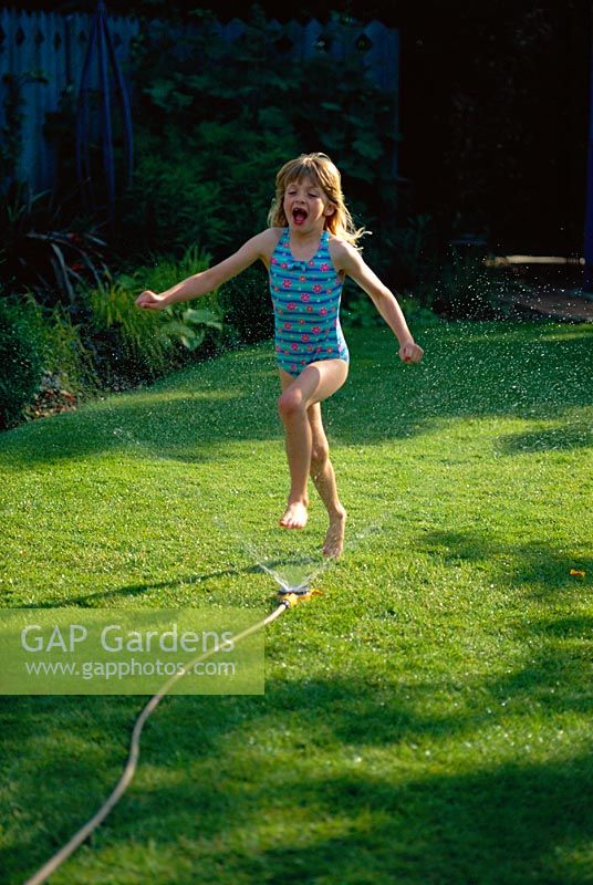 Jeune fille jouant avec un tuyau d'arrosage dans le jardin