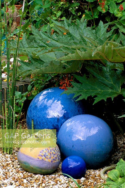 Une cruche de salamandre de Barcelone et des boules de cobalt bleu dans du gravier dans le jardin de style balnéaire de Robin Green et Ralph Cade, Londres