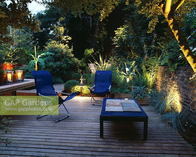 Terrasse en bois avec éclairage, chaises de terrasse en bois bleu, table en bois avec bougies, Musa basjoo et Agave