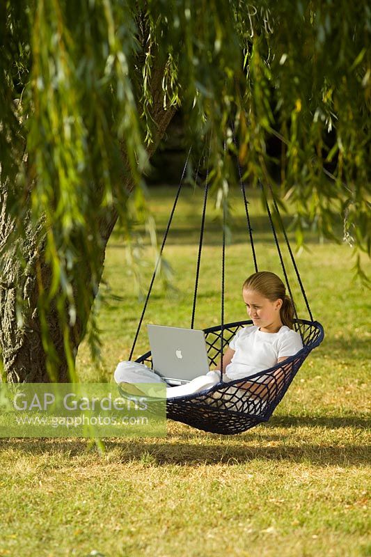 Adolescente assise sur un fauteuil suspendu avec ordinateur portable