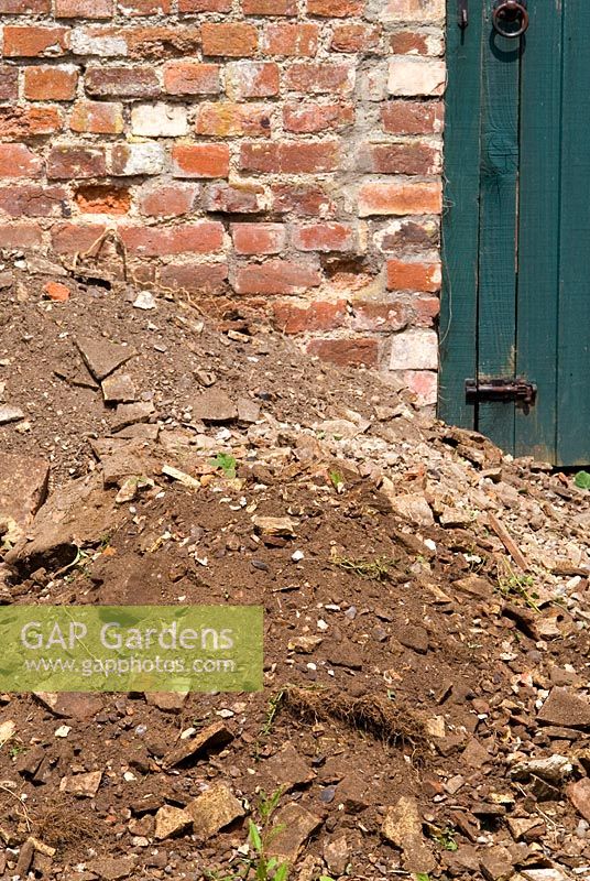 Tas de vieux gravats avec de vieilles briques, un sol pauvre et des racines en attente d'être enlevés pour faire place à un nouveau jardin