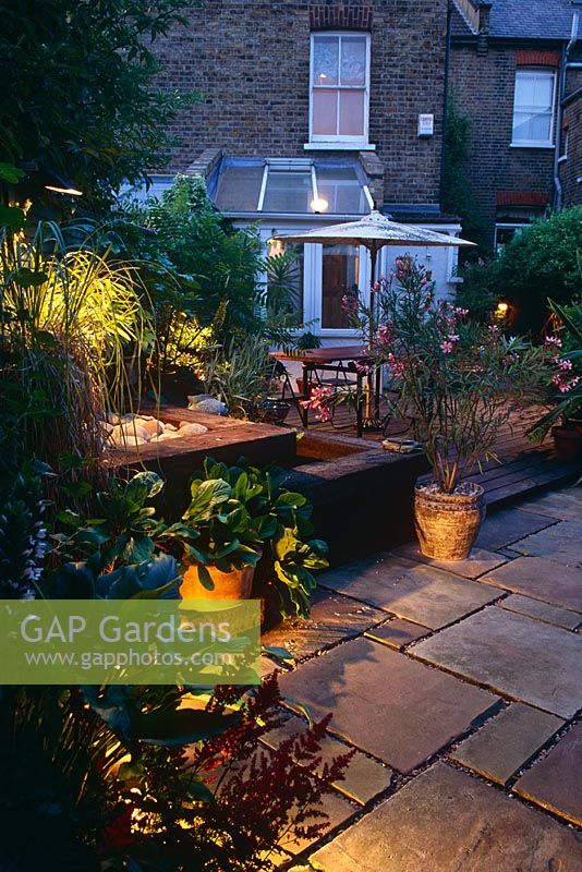 Petit jardin à l'arrière de la ville la nuit avec terrasse pavée avec table et chaises. Traverse de chemin de fer surélevée et pot d'eau de laurier-rose - Londres