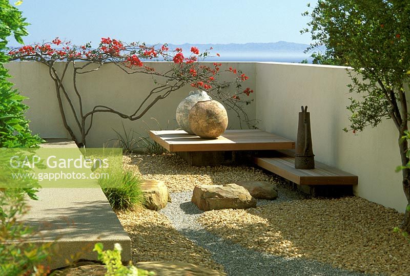 Jardin moderne avec gravier, pierres ornementales, globes et mur peint avec des fleurs rouges grimpantes - Santa Barbara, USA