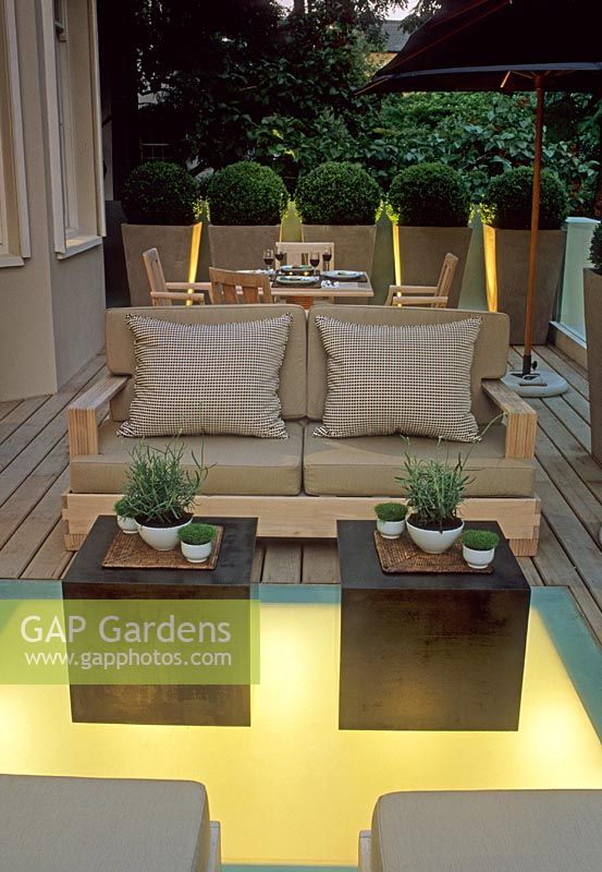 Terrasse en bois contemporaine avec éclairage au sol, tables de style oriental, canapé avec coussins et pots de sphères Buxus topiarisées - Kensington, Londres