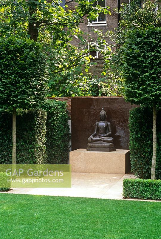 Statue de Bouddha comme point focal dans le jardin de la ville formelle avec pelouse et arbres blanchis - Kensington