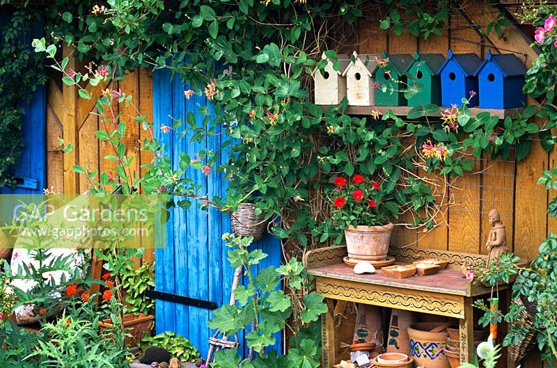 Un pavillon d'été en bois avec des plantes mélangées et des nichoirs peints à l'extérieur