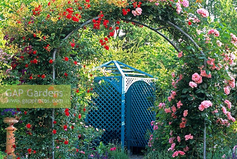 Une arche couverte de roses errantes menant à un pavillon