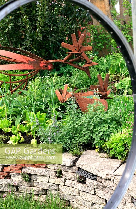 Jardin construit à partir de matériaux recyclés - Fenêtres fabriquées à partir de roues de vélo, sculptures de poulet fabriquées à partir de vieilles pièces de tondeuse et sous-plantées de légumes et d'herbes
