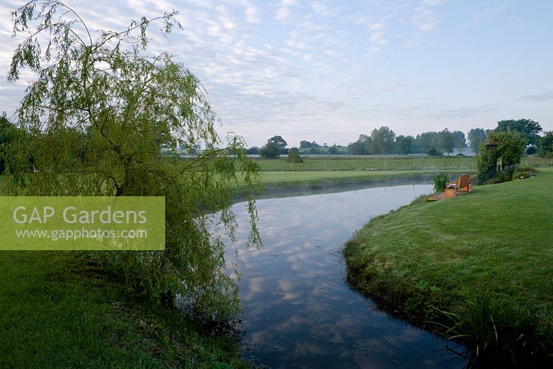 Ciel reflété dans l'eau - vue sur l'étang jusqu'aux marais où les saules sont cultivés pour le tissage. Salix x sepulcralis var. chrysocoma - saule pleureur au premier plan