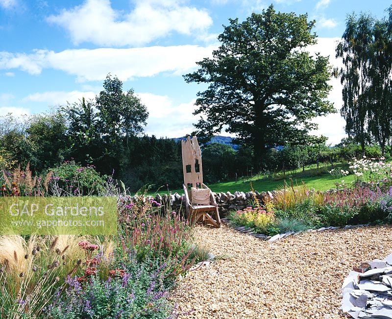 Le jardin de gravier, le mur et la chaise en bois 'Trône' avec les collines noires derrière