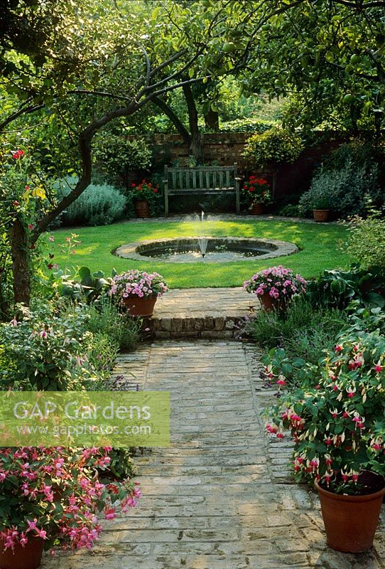 Petit jardin clos de ville avec pelouse hexagonale, plan d'eau et chemin de granit. Pots avec Fuchsias et Impatiens - Londres