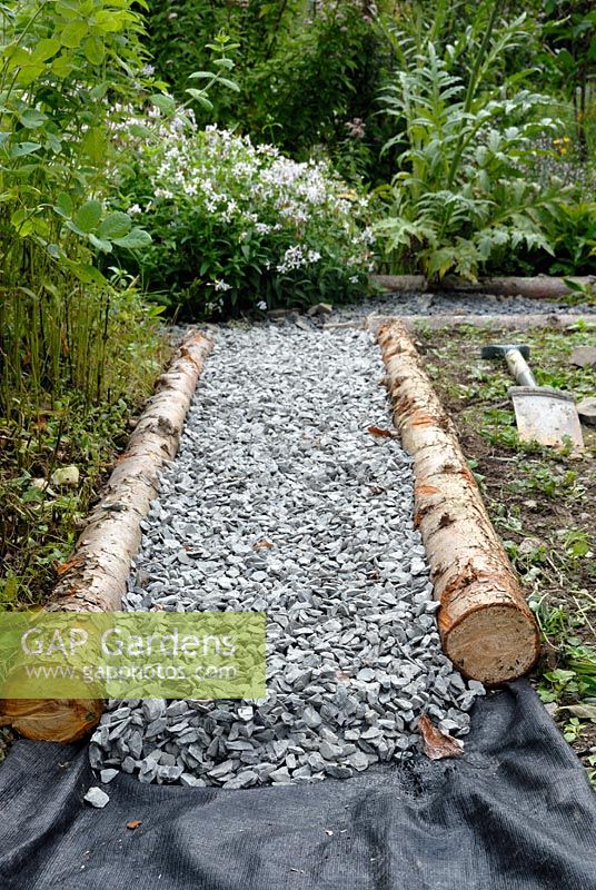 Pose d'un chemin de jardin avec une membrane de contrôle du bois rustique, du gravier et des mauvaises herbes