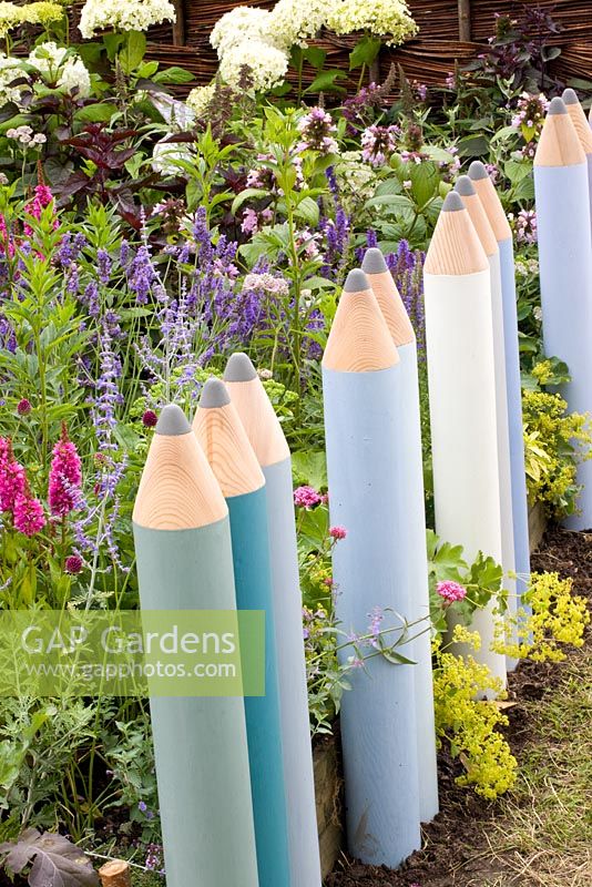 Clôture faite de crayons de couleur géants à côté de parterres de fleurs