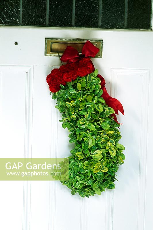 Bas de Noël sur la porte d'entrée remplie de mousse et recouvert de petits brins d'euonymus à feuilles persistantes et d'œillets en aérosol rouge
