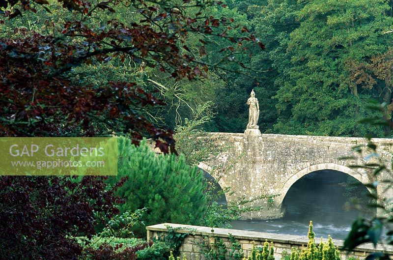 Pont sur la rivière Frome entrevu du jardin et distingué par une figure de Britannia - Iford Manor, Bradford-on-Avon, Wiltshire