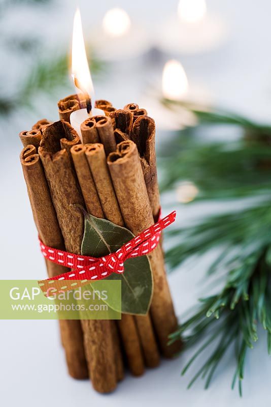 Décoration de Noël simple avec un paquet de bâtons de cannelle attachés autour d'une bougie avec un ruban rouge et une feuille de laurier