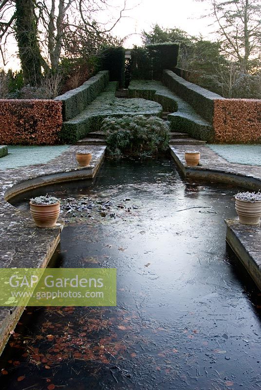 Des cadres de coupe fortement coupés montent vers le Temple des quatre vents du jardin rouge avec un étang formel en son centre contenant un bouquet de Cyperus alternifolius - Kingston Maurward Gardens, Dorchester, Dorset