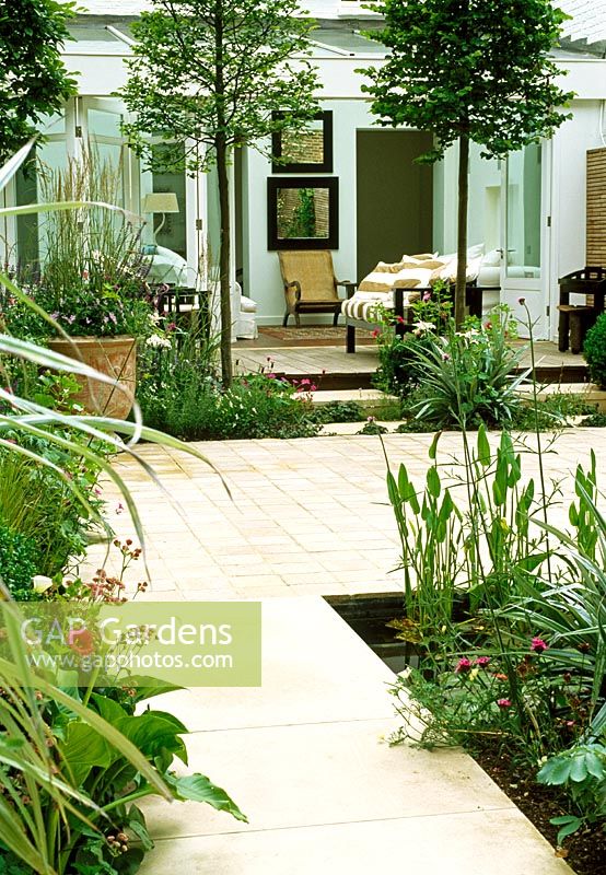 De cet appartement de jardin meublé vert pâle, des portes coulissantes s'ouvrent sur une cour intérieure. L'espace est divisé par des charmes blanchis, des planches de vivaces délicates et un étang en forme de stip.