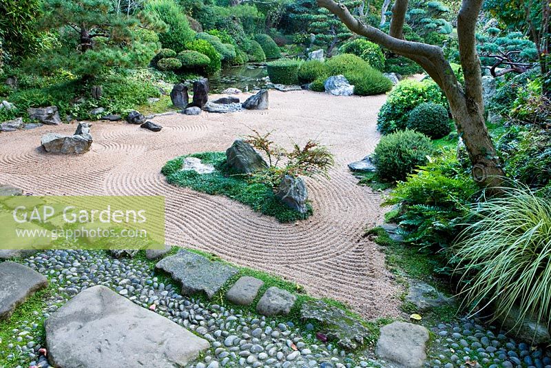 Le jardin de gravier de méditation zen avec des rochers, du gravier ratissé, une piscine, 'l'île aux grues' à gauche, 'l'île aux tortues' à droite avec Cotoneaster horizontalis - Jardin de style oriental, France
