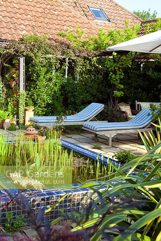 Jardin d'inspiration marocaine avec plantation tolérante à la sécheresse étang carrelé et bateaux à vapeur en bois sur la terrasse