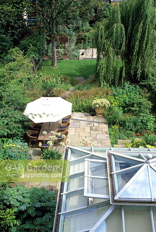 Conservatoire qui s'ouvre sur une terrasse pavée en pierre, offrant un coin repas extérieur, bordé d'une plantation douce - Islington, Londres