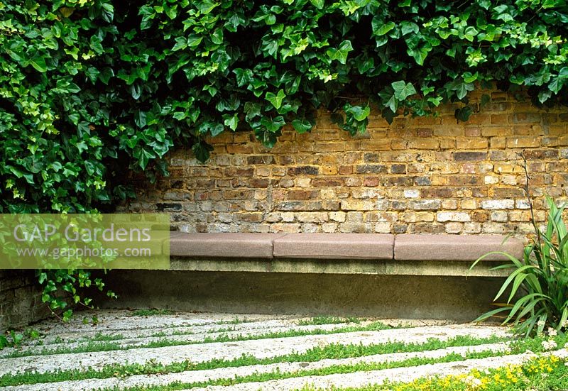 Un coin salon à l'arrière du jardin. Le lierre verdit le mur, des bandes alternées de béton texturé et de sedum créent le sol