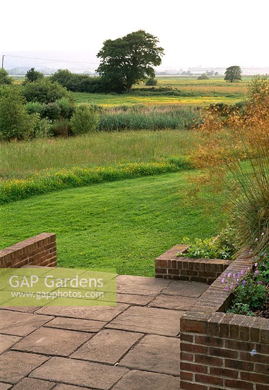 Une terrasse inférieure s'ouvre sur une vue imprenable sur les prairies d'eau de ce jardin du Sussex