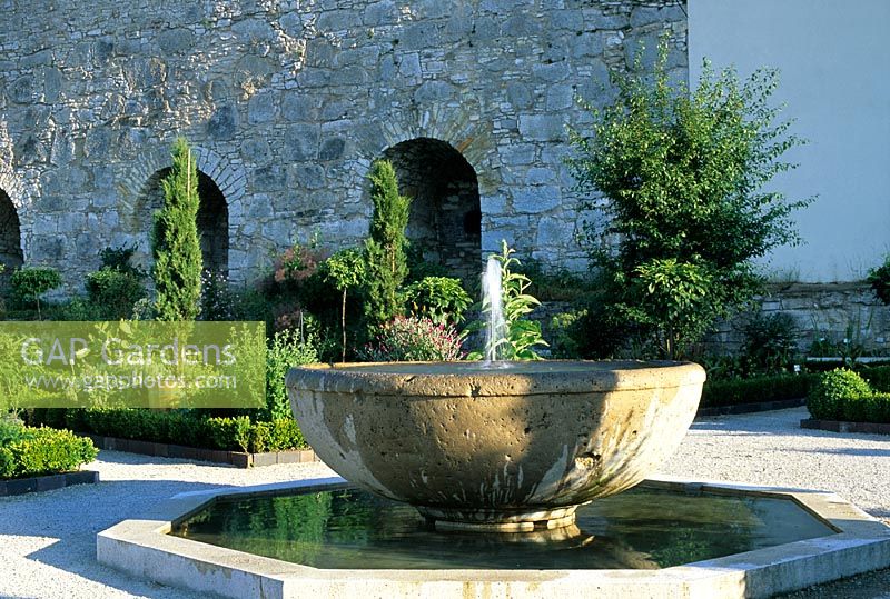 Fontaine d'eau coulant dans la piscine hexagonale, petits parterres rectangulaires avec plantation mixte et chemins de gravier - Cour d'Hortus Eystettensis