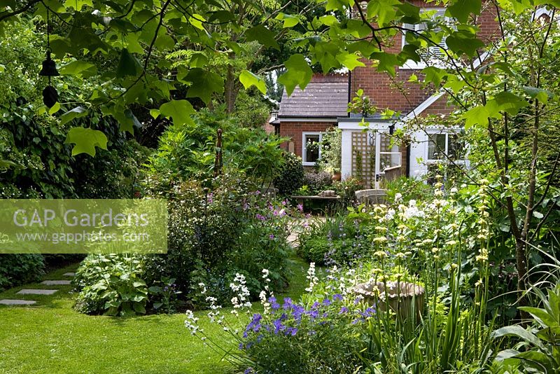 Regardant le jardin vers la maison encadrée par les feuilles Liriodendron tulipifera, courbant la pelouse et les parterres de fleurs - Eldenhurst
