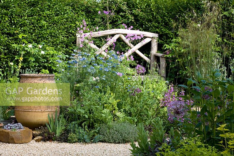 Banc en bois dans la zone de gravier avec une urne en terre cuite vide avec Nigella, Alliums et Geranium plamatum - Eldenhurst