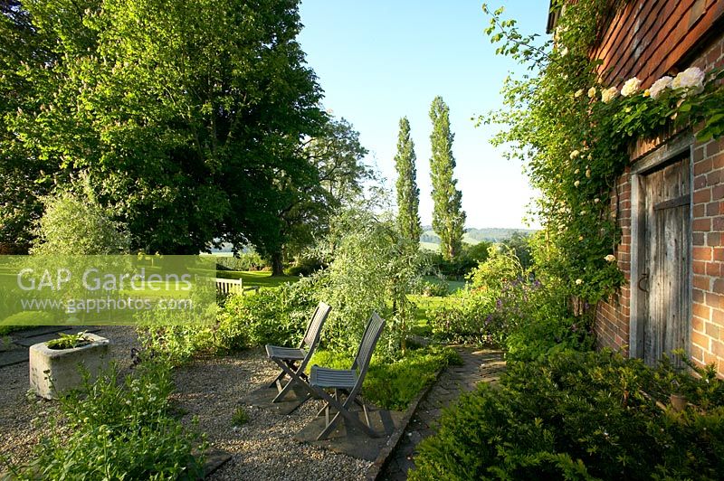 Patio en gravier, avec deux chaises en bois donnant sur le jardin et la campagne de l'East Sussex, tôt le matin
