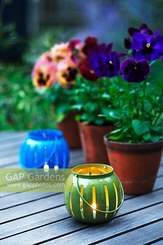 Pensées dans des pots en terre cuite sur une table de jardin en bois avec des bougies chauffe-plat au premier plan