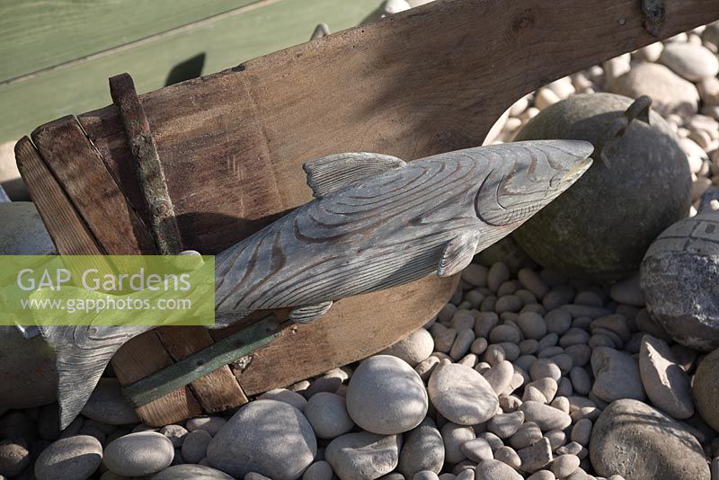 Jardin inspiré de la mer. Détail de poissons sculptés sur bois sur la plage de galets.