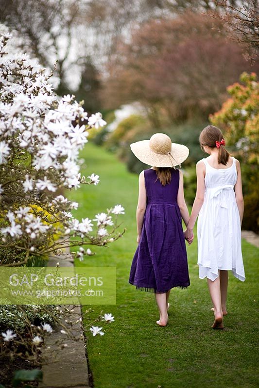Deux jeunes filles portant des robes d'été marchant le long d'un chemin d'herbe entre les parterres d'arbustes et de Magnolia