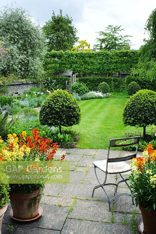 Vue de la terrasse et du jardin au printemps, siège de jardin pliant vintage, pots de fleurs murales, vue sur la pelouse avec boîte topiaire
