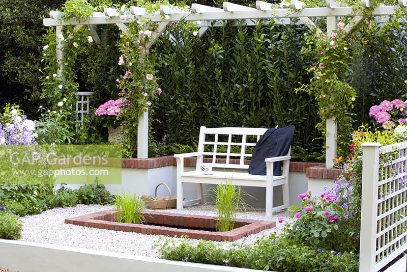 Petite cour en gravier avec assise en bois sous pergola, piscine et parterres colorés. Le jardin 'Christian avant Dior' - Médaillé de bronze au RHS Chelsea Flower Show 2010