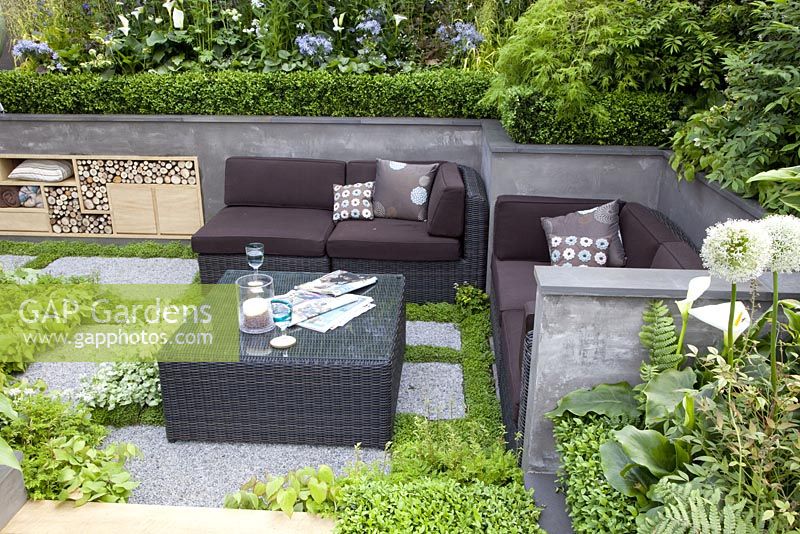 Terrasse en contrebas avec table basse et canapé en osier. Jardin 'A Joy Forever', médaillé d'argent au RHS Chelsea Flower Show 2010