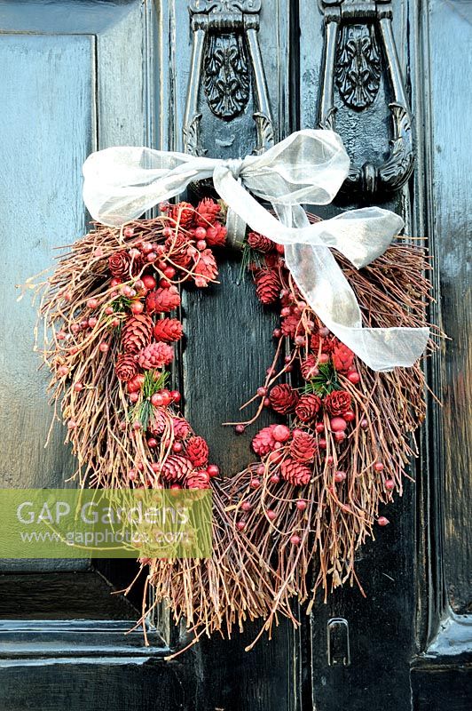 Couronne d'automne de pommes de pin et de baies, attachée avec un ruban blanc, suspendue à un heurtoir de porte en fonte