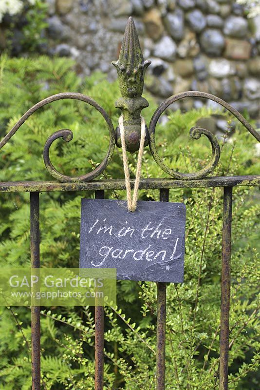 Panneau en ardoise sur le portail en fer forgé, indiquant 'Je ' m dans le jardin'