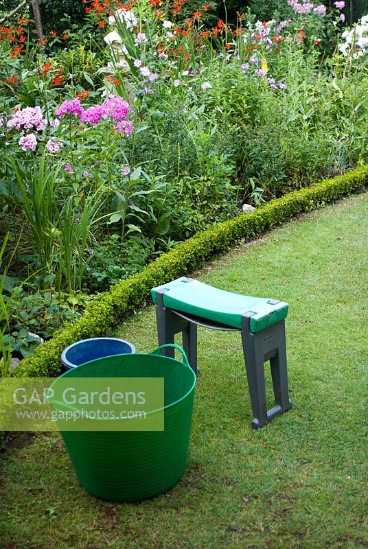 Tubtrug - baignoire de jardin en plastique avec poignées - et à genoux sur la pelouse avec parterre de fleurs herbacées d'été bordé par Buxus coupé