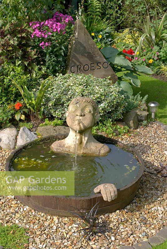 Une pièce d'eau à demi-baril avec bec et mains submergés, cadran d'horloge en plateau de table orné peint et sculpture en pierre sculptée avec 'Croeso' - bienvenue en gallois à 'Trevinia', Stubbins, Lancashire NGS