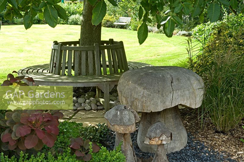 Banc circulaire sous arbre et champignons ornementaux en bois. Parsons Cottage, Essex, Royaume-Uni
