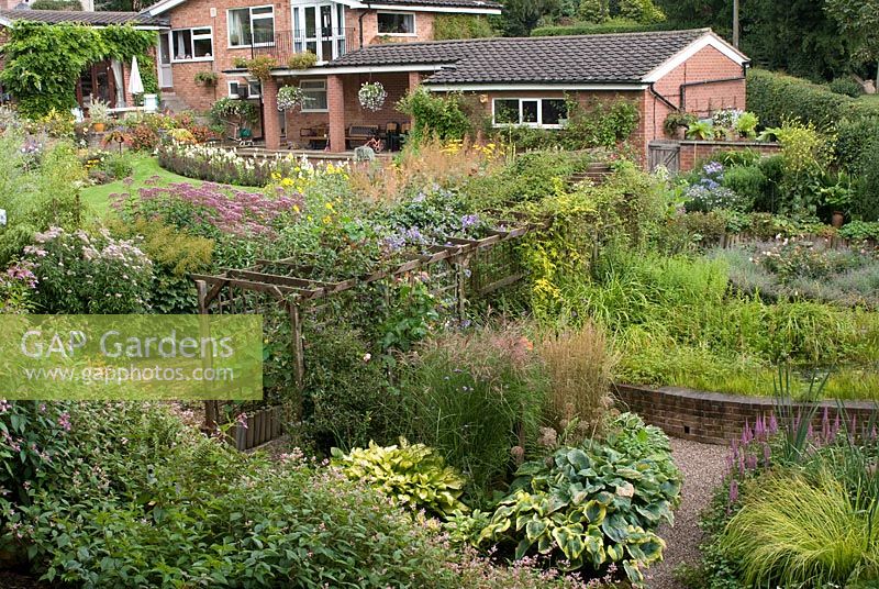 Portrait de maison et jardin arrière avec étang rasied, jardin de tourbière, pergola, terrasse et parterres de fleurs herbacées à la fin de l'été à 'Springbank', Davenham, Cheshire NGS