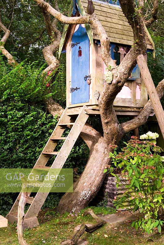Maison dans les arbres d'influence gothique au milieu de branches parsemées de masques et d'oiseaux. Le jardin secret de Serles House, Wimborne, Dorset, UK