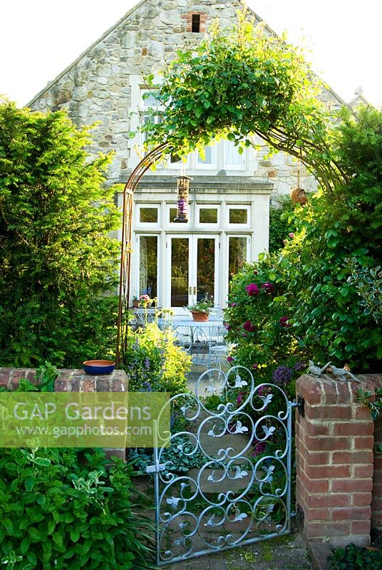 Porte métallique décorative reliant le potager clos avec le patio à l'extérieur de la cuisine, avec Rosa rouge foncé 'Roseraie de l ' Hay' - Old Presbytère, Kingston, île de Wight, Hants, UK
